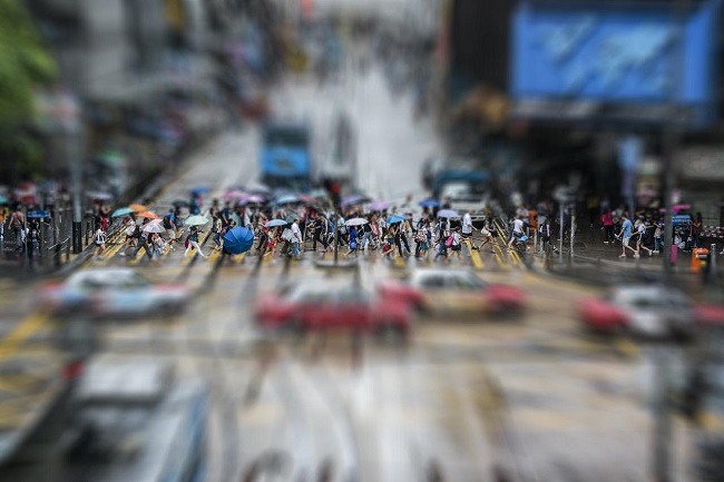 Pedestrians, many carrying umbrellas, crossing a busy intersection in a city with traffic all around